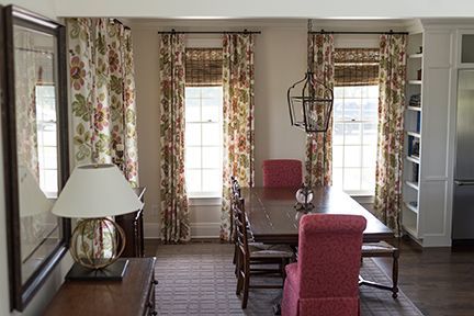 Dining room with wood table, red chairs, floral curtains, and a large mirror.