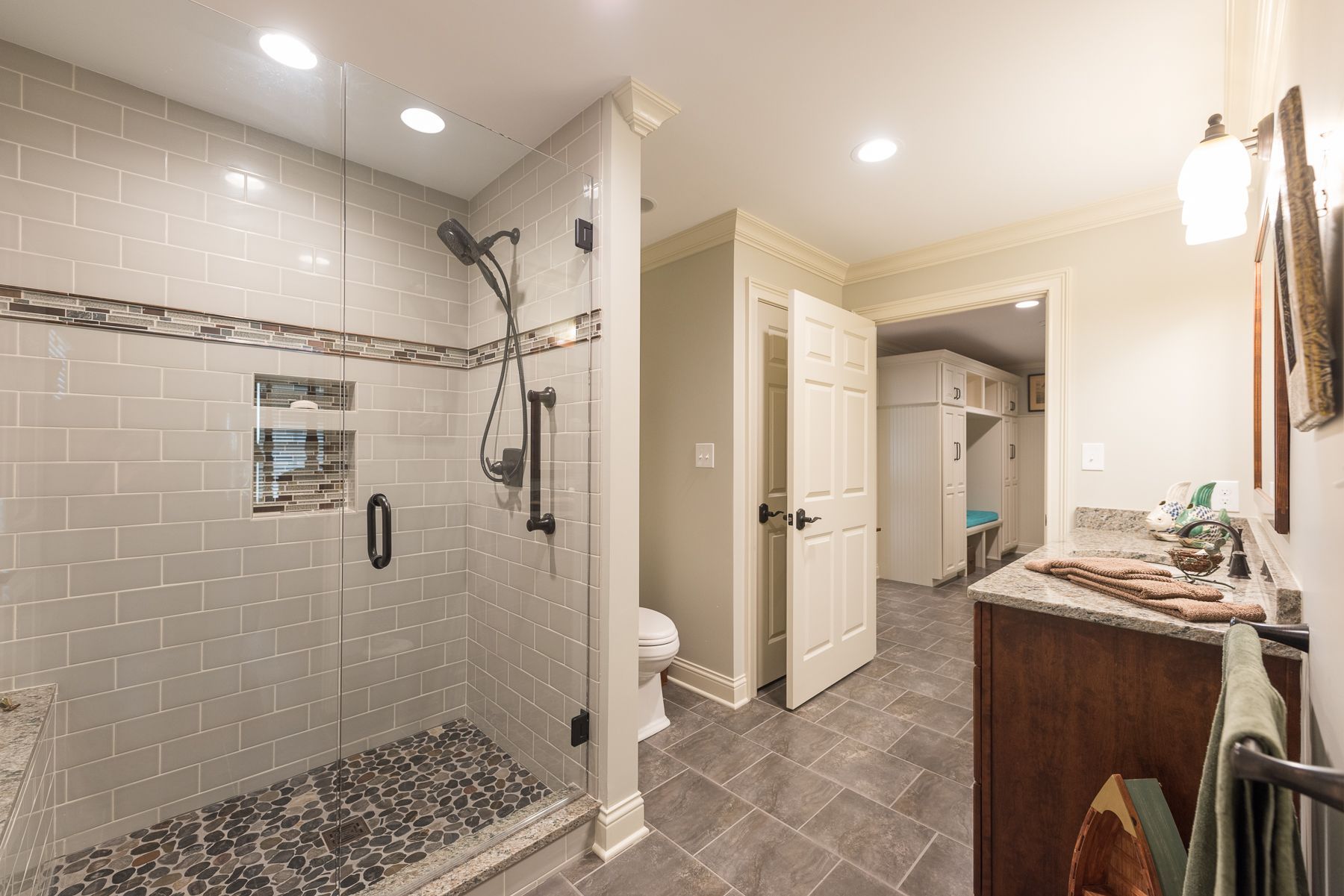 Bathroom with gray tile shower, stone floor, vanity, and open door to a closet.