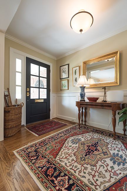 Entryway with a colorful rug, black door, and a table with a mirror and lamp.