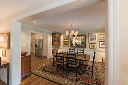 Dining room with table, chairs, rug, artwork, and chandelier; pale green walls, wood floor, and white trim.