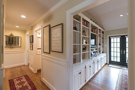 Hallway with built-in shelving, white cabinets, and a dark door leading outside; hardwood floor and white trim.
