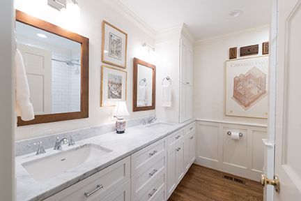 Bright white bathroom with a long vanity, two sinks, and framed art.