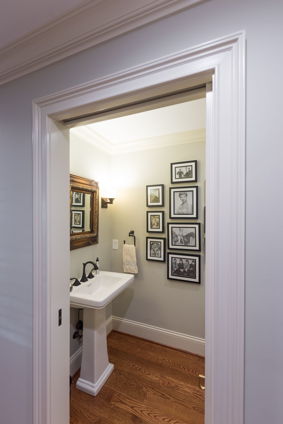 A small powder room with a pedestal sink and a gallery of black and white photos.