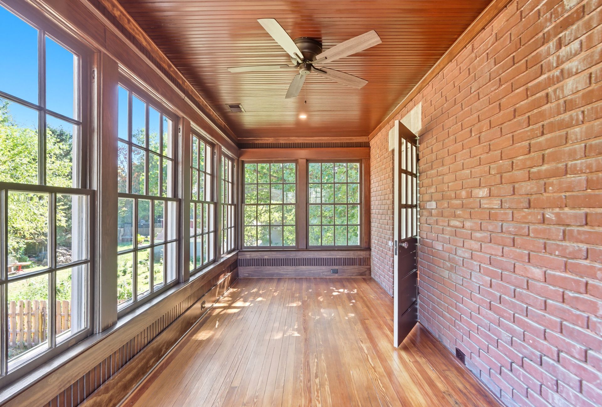 Sunroom with brick wall, windows, wood floor, and ceiling fan.
