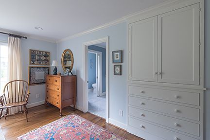 Bedroom with blue walls, wood floor, rug, chest of drawers, built-in cabinets, chair, and open doorway.
