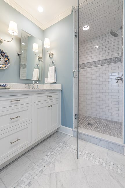 Bathroom with white vanity, blue wall, glass shower, and patterned floor.
