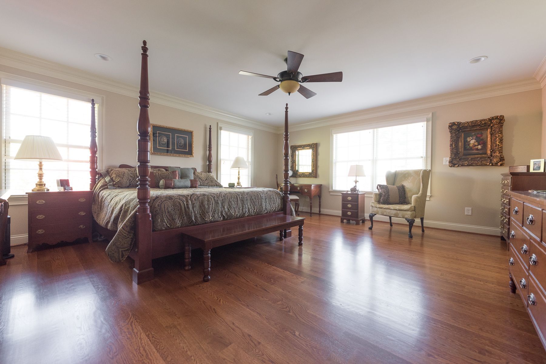 Spacious bedroom with a four-poster bed, hardwood floors, and windows; neutral color palette.