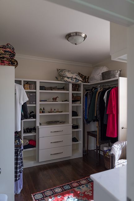 White closet with shelves, drawers, and hanging clothes in a room with a rug.