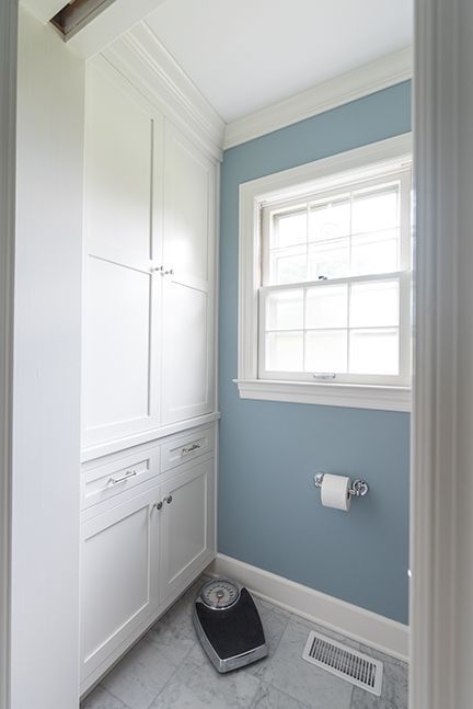 Small bathroom with blue walls, white cabinets and trim, and a window with a toilet paper roll.