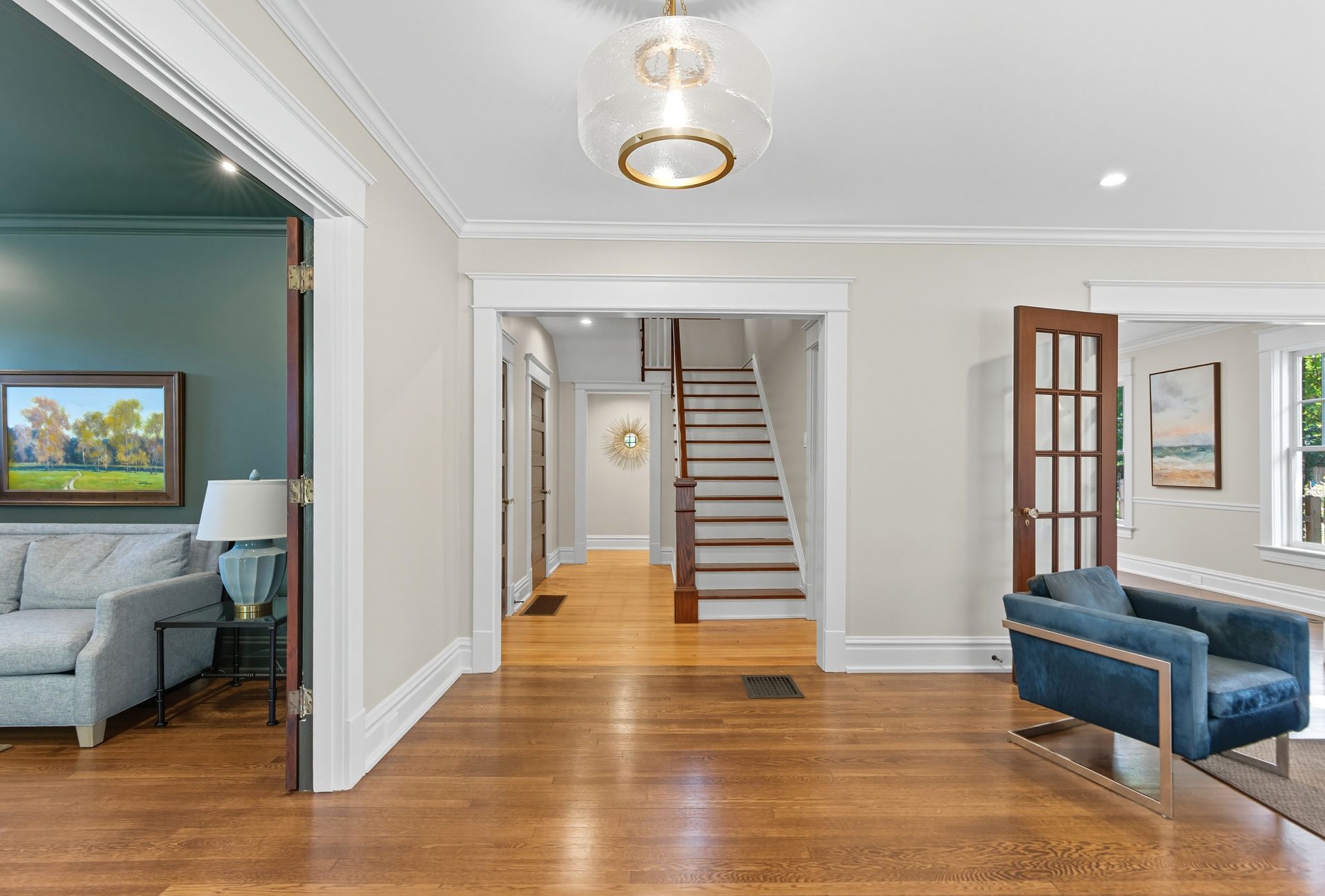 Interior shot of a bright home entry with hardwood floors, a blue chair, and stairs leading up.