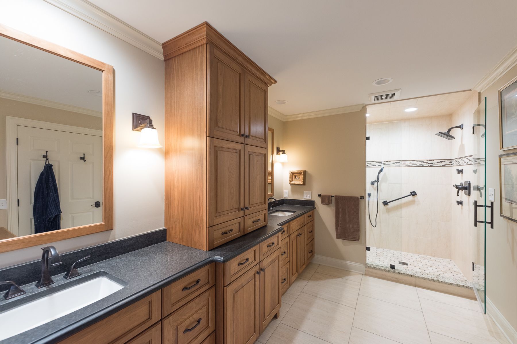 Bathroom with wood cabinets, dark countertops, shower with glass door, and large mirror.