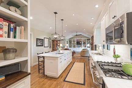 Spacious kitchen with white cabinets, island, and stainless steel appliances, leading into a living area.