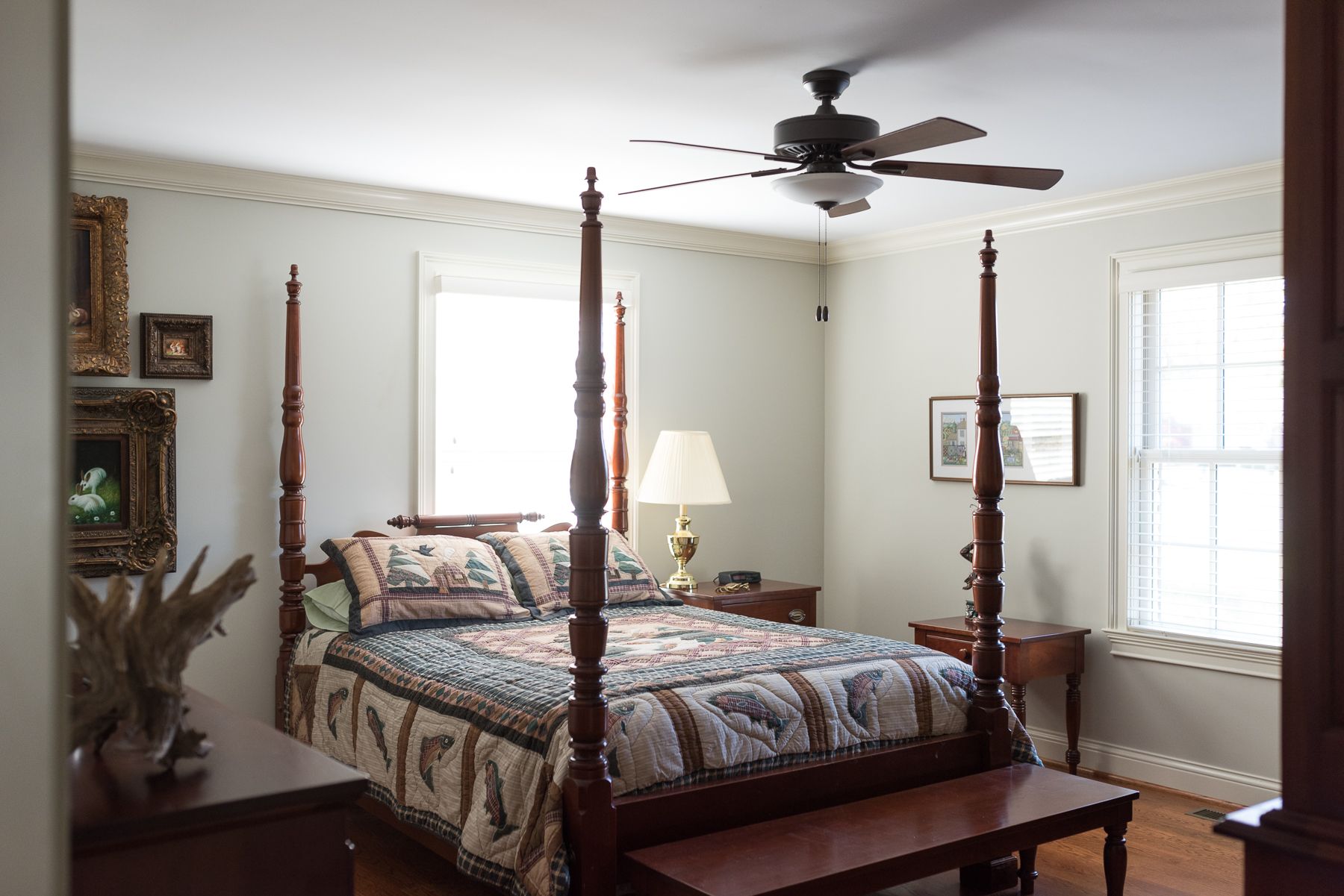 Bedroom with four-poster bed, floral quilt, two windows, and decorative trim.