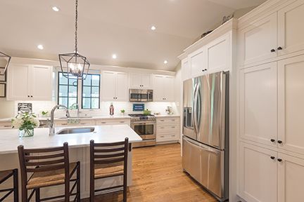 Bright white kitchen with stainless steel appliances, wooden floors, and a center island with bar stools.