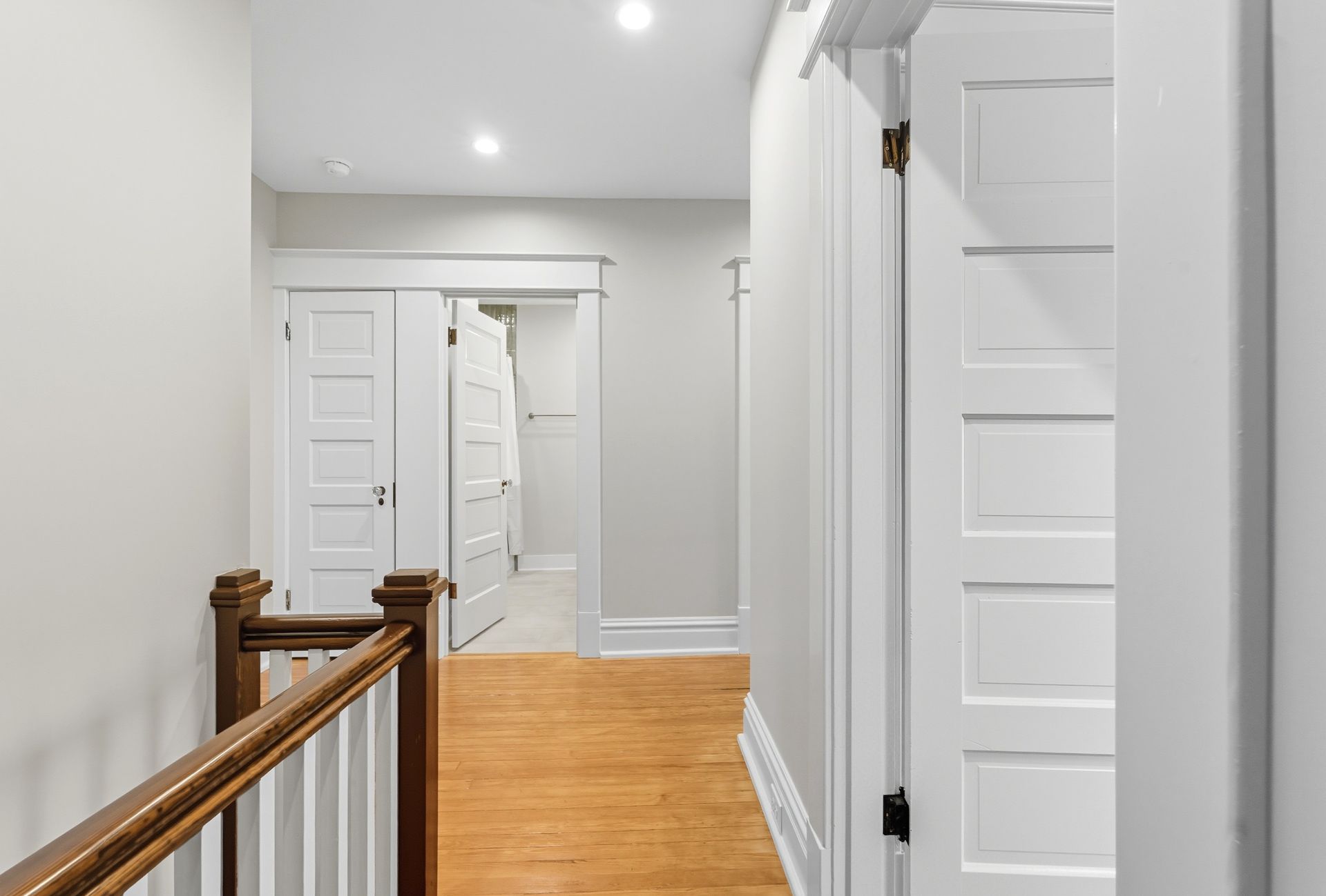 Hallway with white doors, wood floor, and a wooden railing.