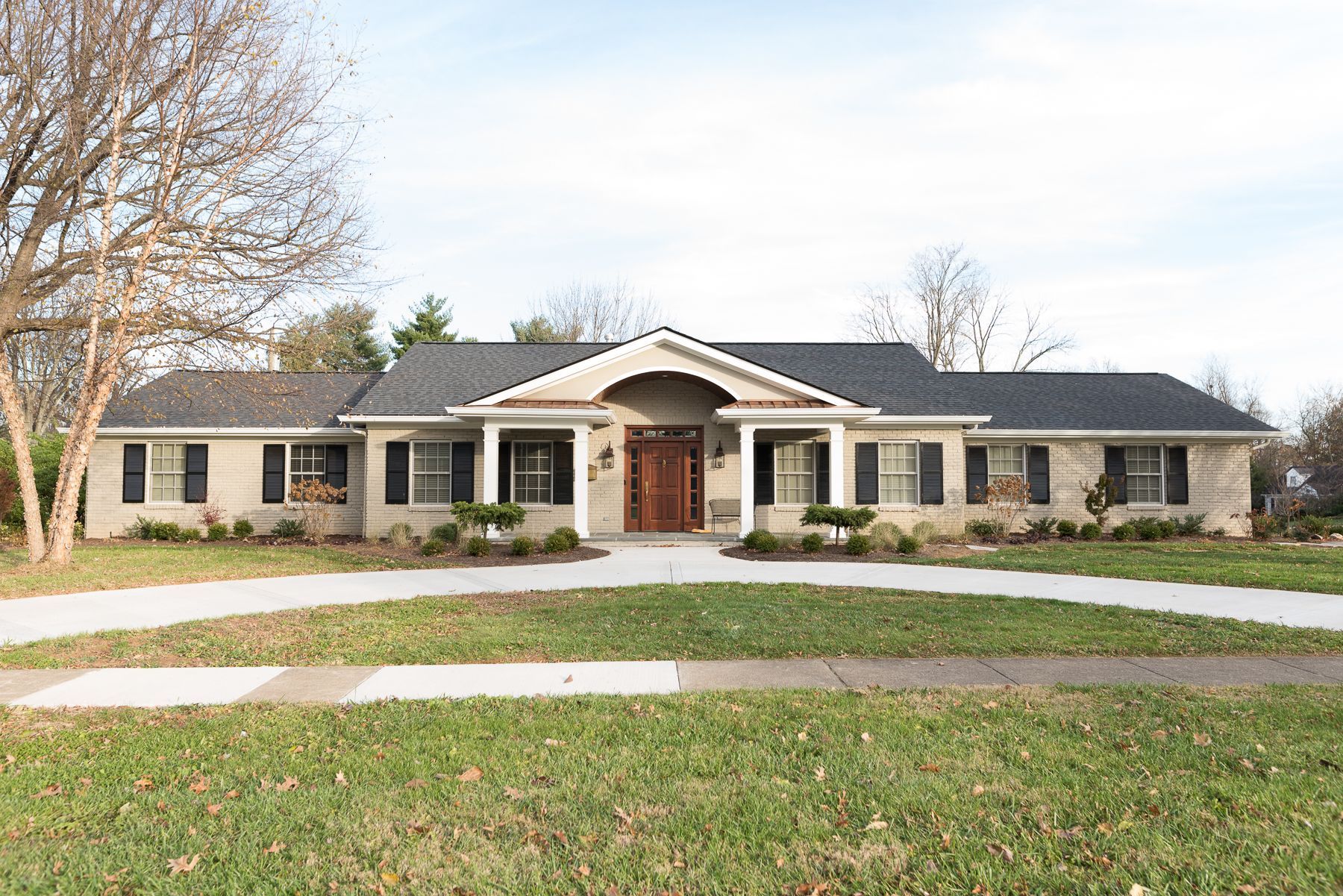 Ranch-style home with a circular driveway and black shutters, set on a green lawn on a sunny day.