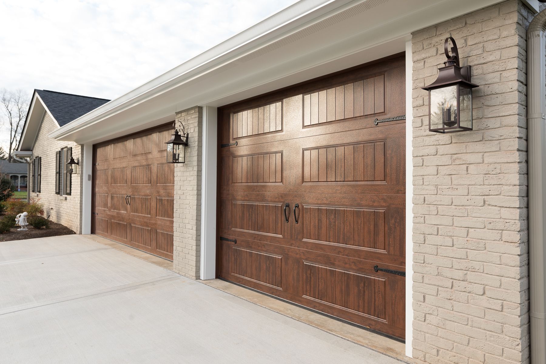Brown garage doors, cream brick building, black lanterns, concrete driveway.