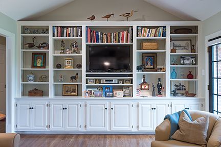 White built-in bookcase with TV, books, and decorative items, in a living room with wood floor.