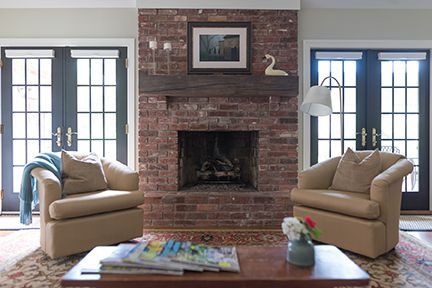Living room with brick fireplace, tan chairs, and French doors.