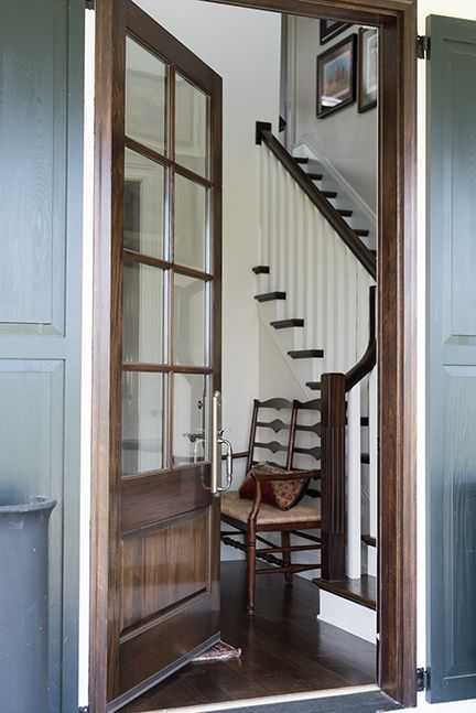 Open wooden door reveals a staircase. A chair sits below. Dark wood and neutral tones dominate.