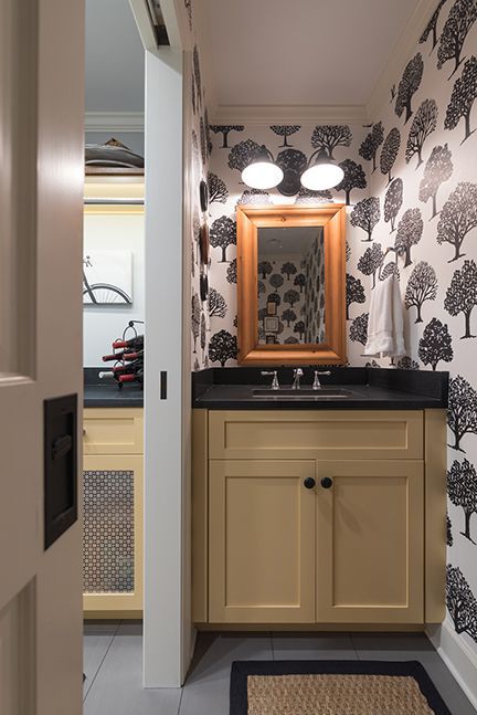 Small powder room with tree-patterned wallpaper, beige vanity, black countertop and mirror, and sliding door.