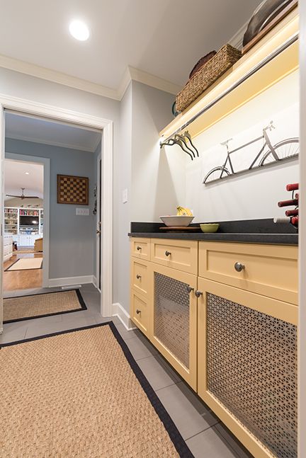 A laundry room with light yellow cabinets, a dark countertop, and a woven mat.