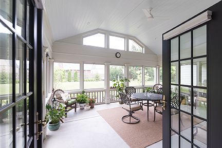 Sunroom with glass doors and windows, a table, chairs, and plants overlooking a yard.