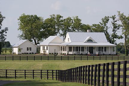White farmhouse with porch and metal roof behind a black wooden fence.
