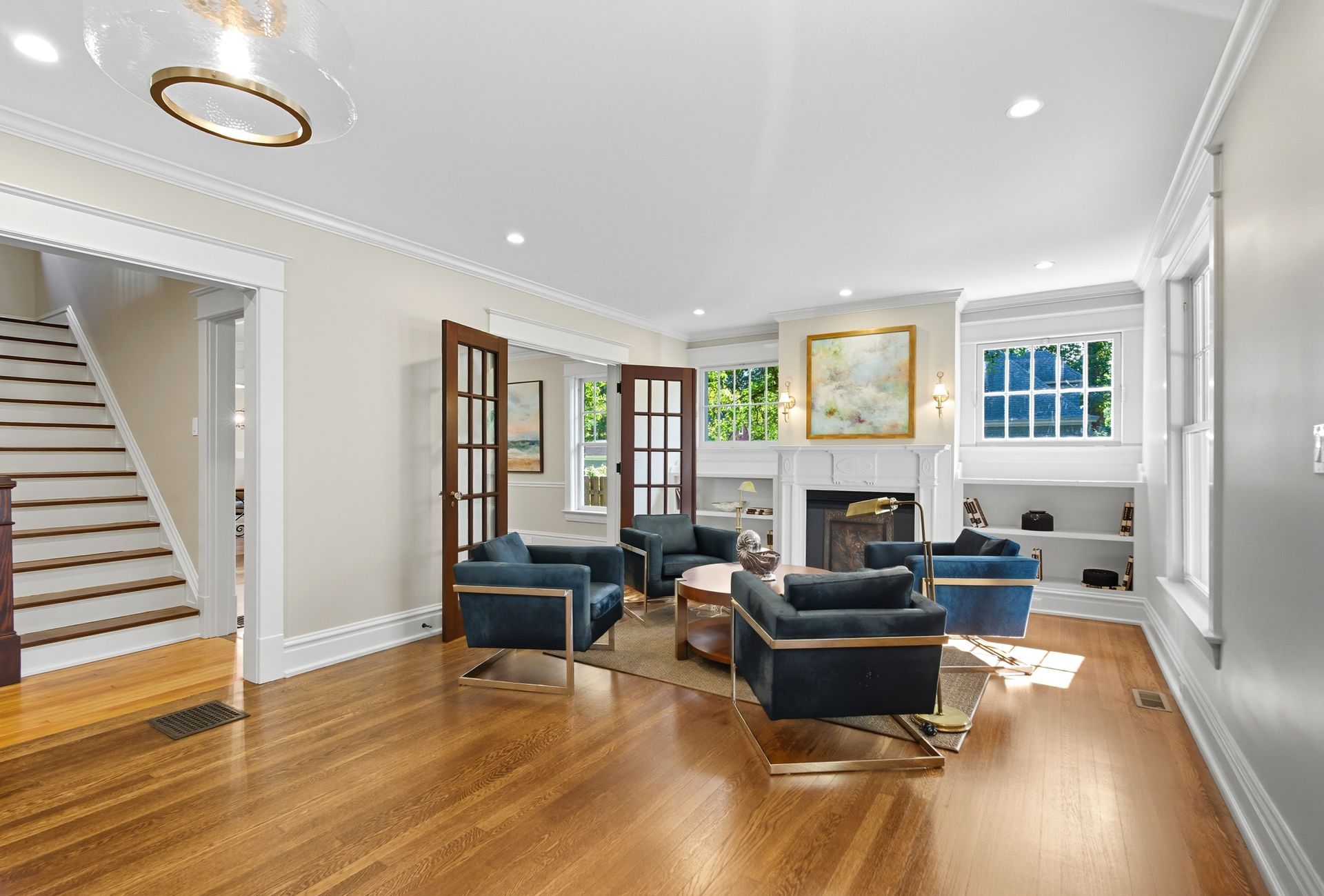 Living room with blue armchairs, fireplace, wood floors, and stairs.