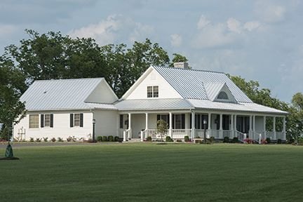 White farmhouse with porch and metal roof, on a green lawn under a cloudy sky.