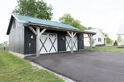 Black barn-style garage with white garage doors, a green roof, and a black asphalt driveway.