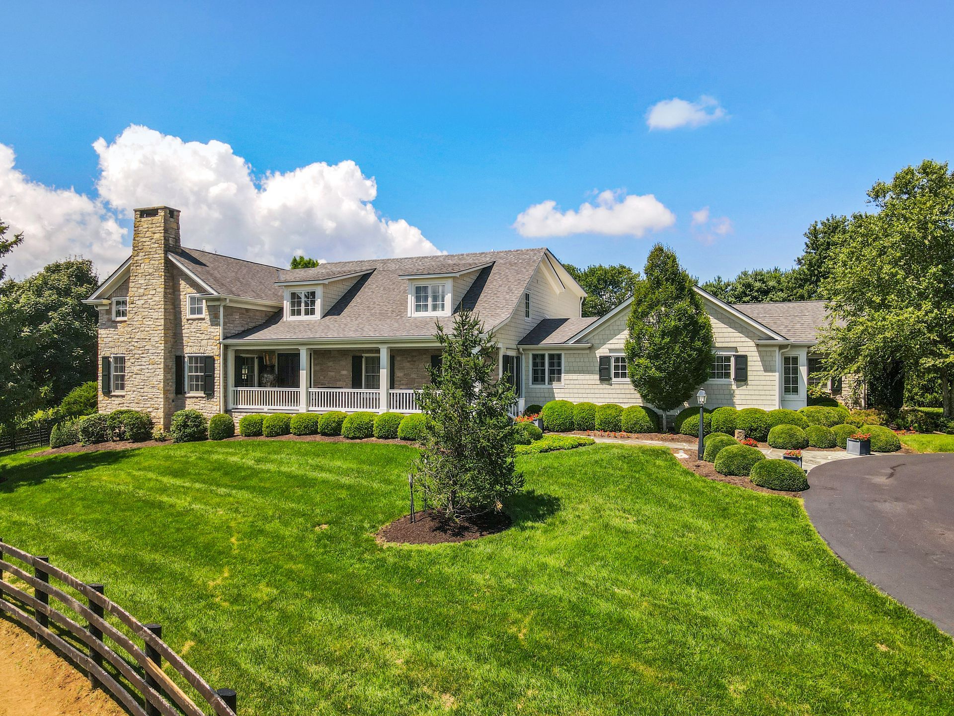 Stone and light green house with large yard, blue sky, and small trees.