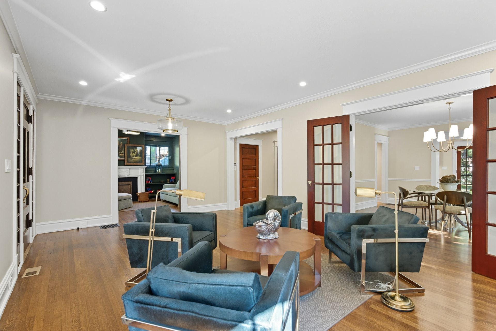 Living room with teal armchairs, round table, wood floors, and red-framed glass doors.