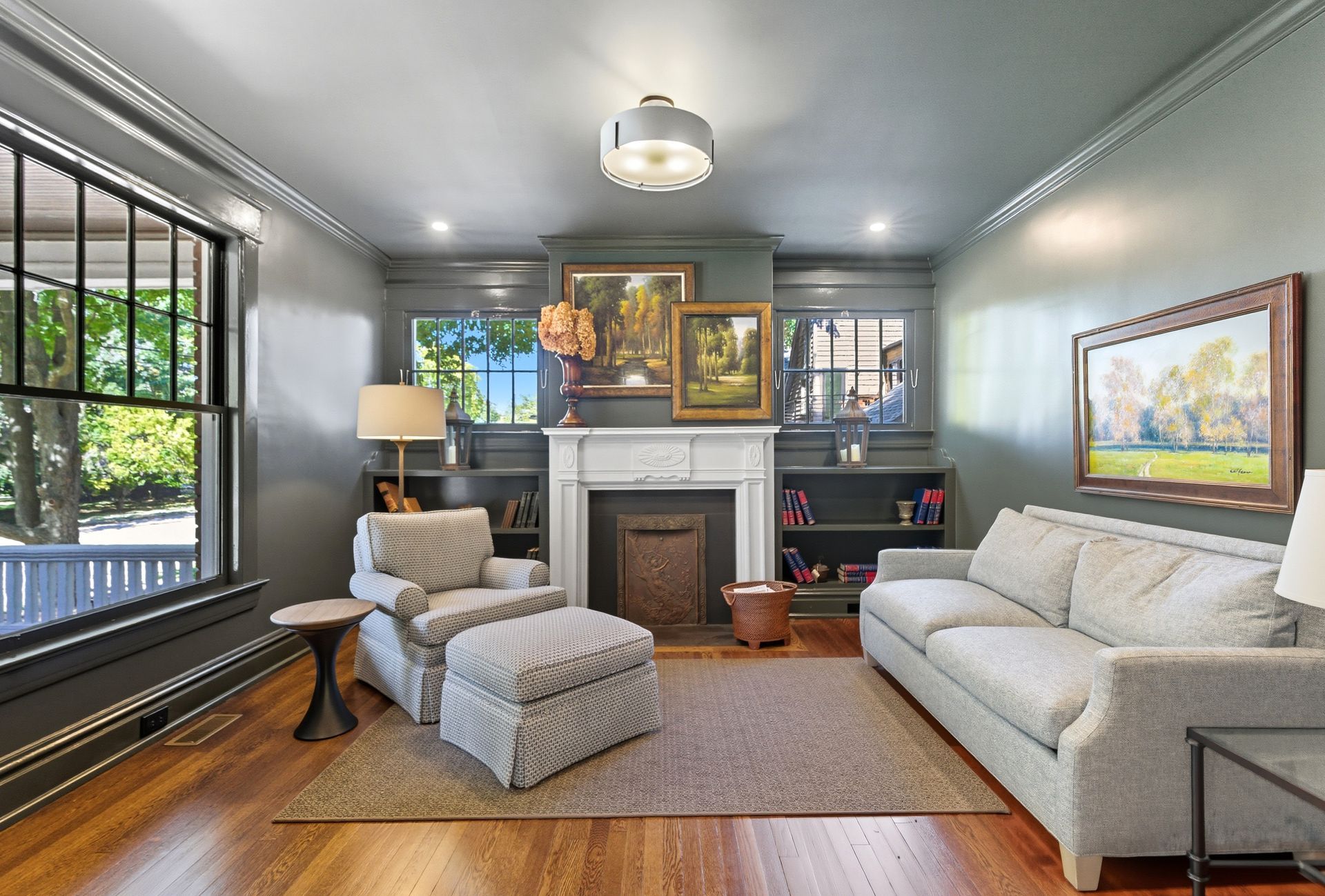 Living room with gray walls, hardwood floors, and artwork over a fireplace.