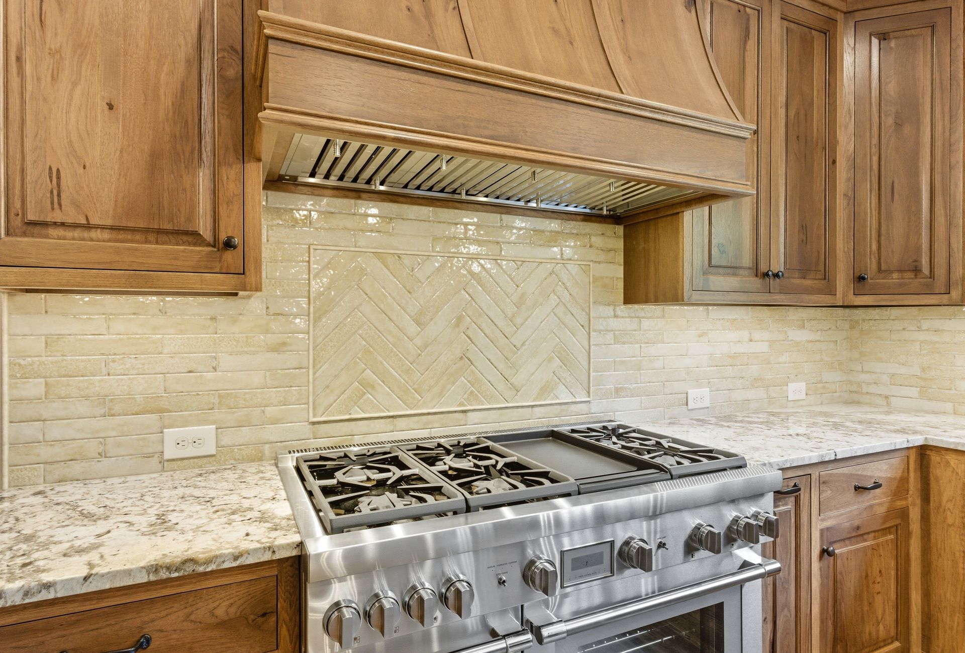 Kitchen with stainless steel range, light wood cabinets, and beige herringbone tile backsplash.