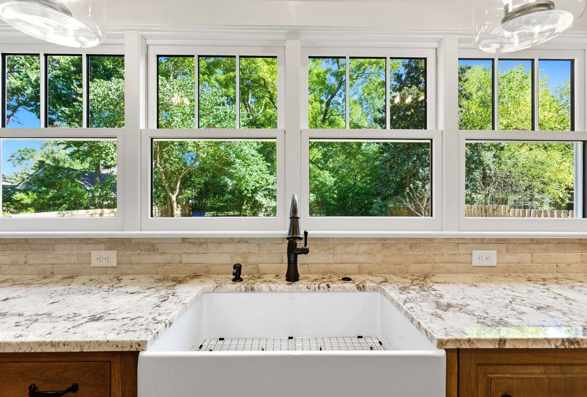 Kitchen sink with window view of trees, granite counters, white sink, and black faucet.