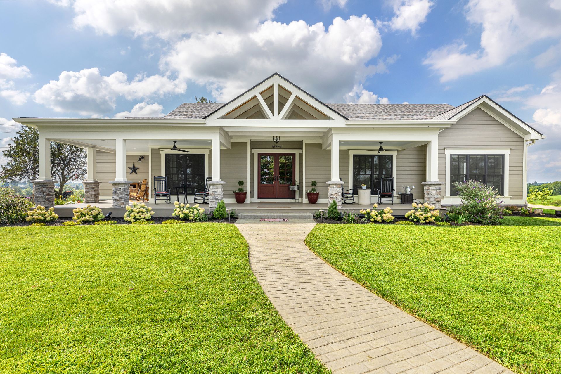 Beige ranch-style house with porch, stone pillars, and brick path on a sunny day.