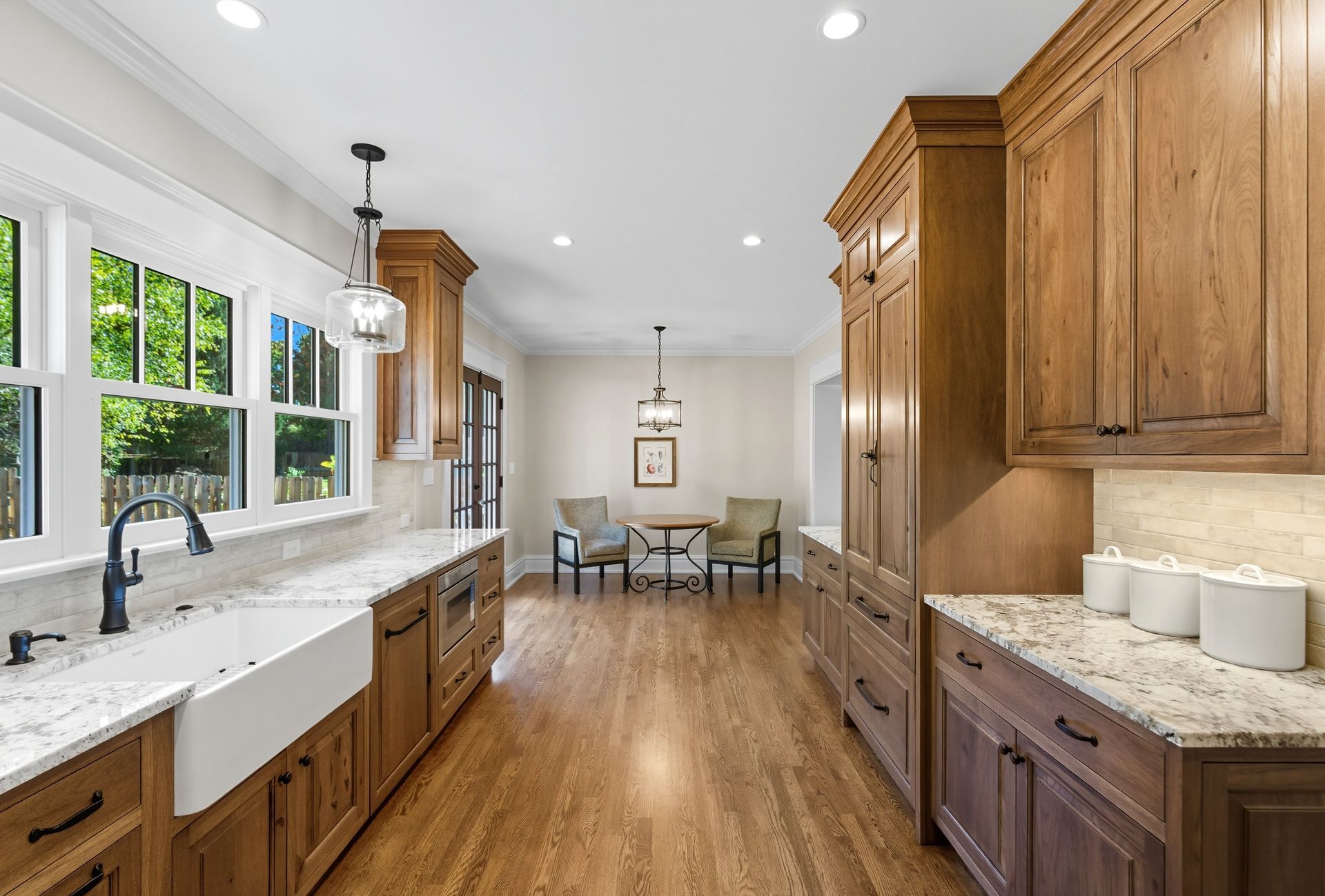 Wooden kitchen with granite countertops, a farmhouse sink, and dining area in the distance.
