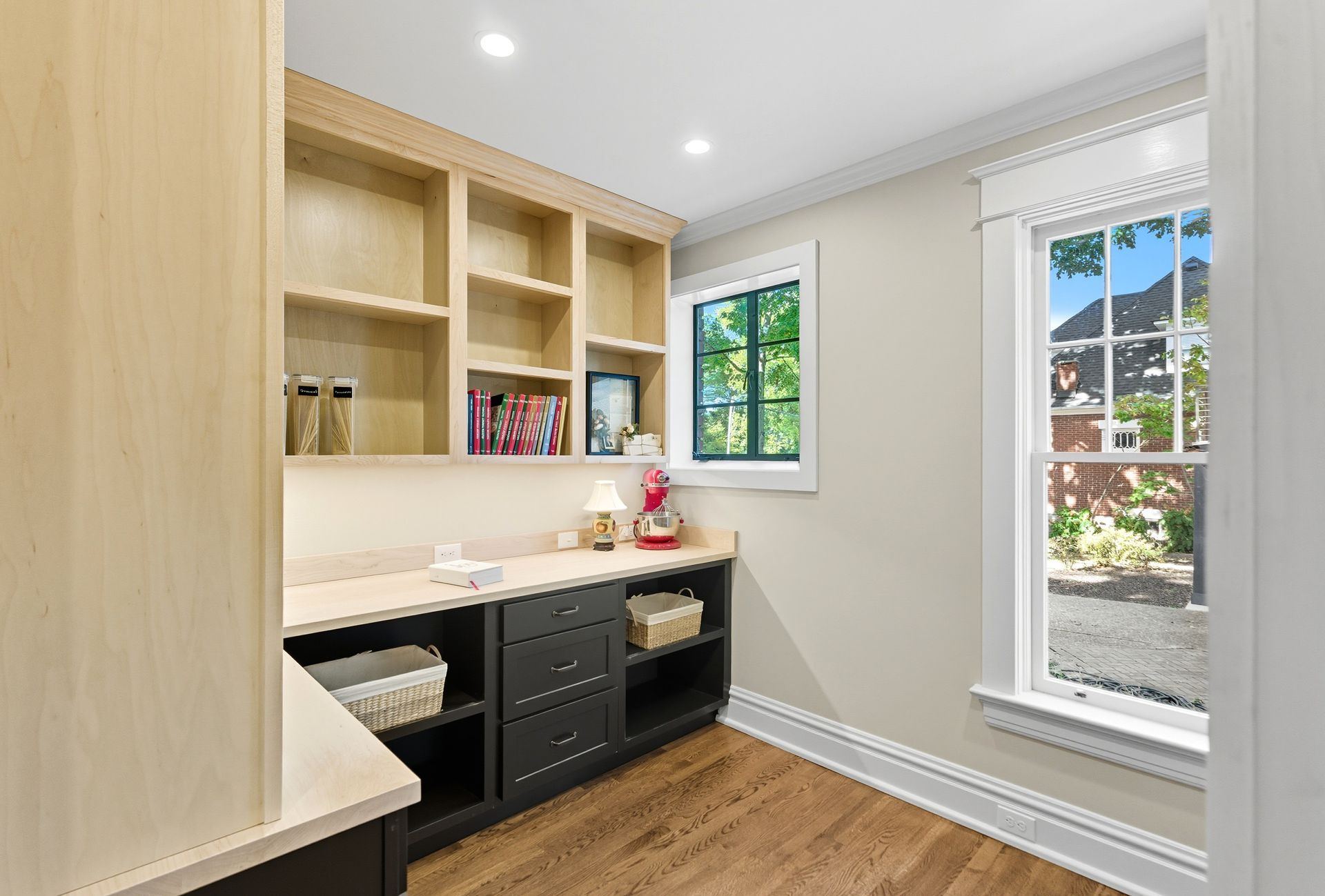 Pantry with wooden shelves, black cabinets, and windows with a view of trees and houses.
