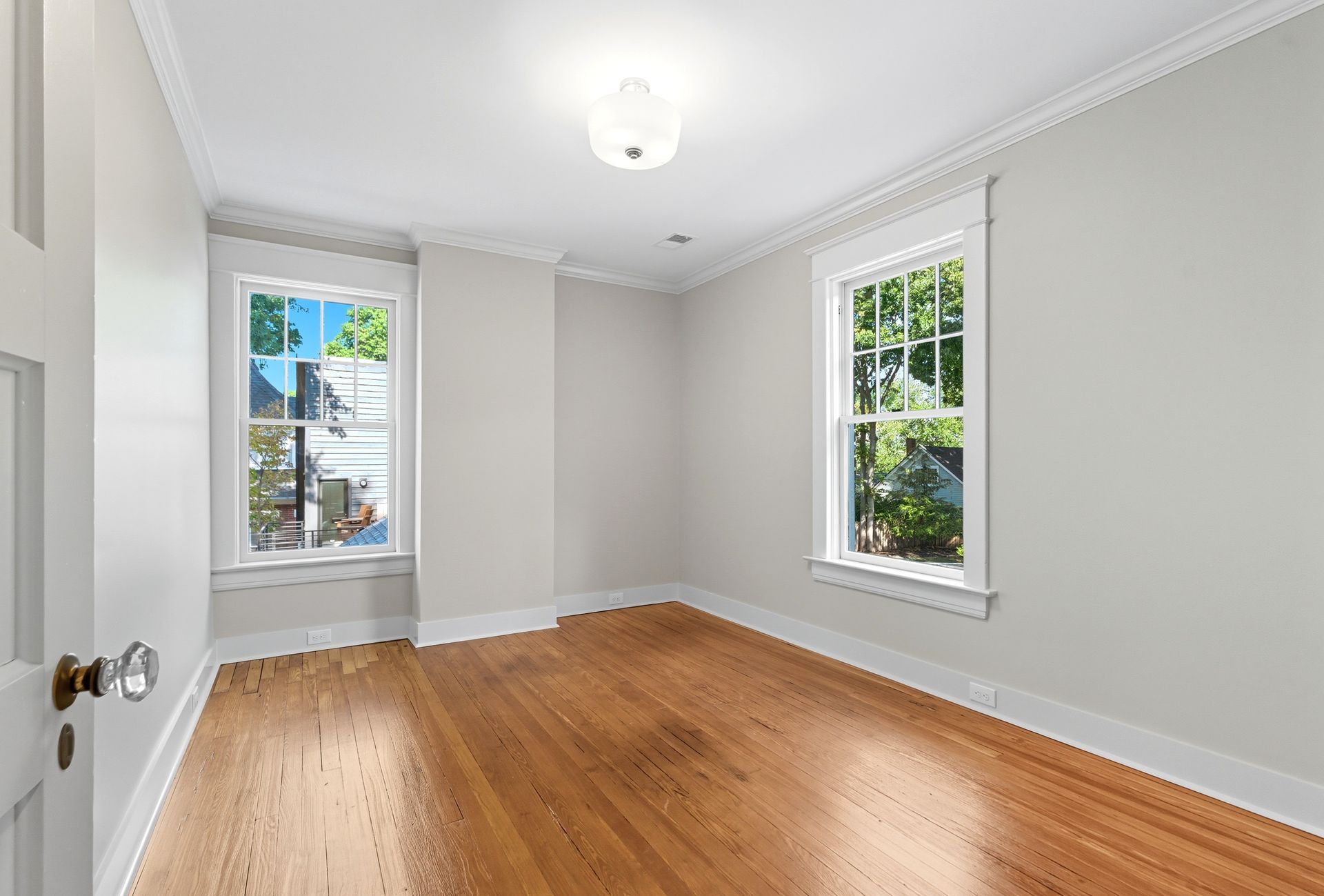 Empty room with hardwood floors, two windows, and a white door.