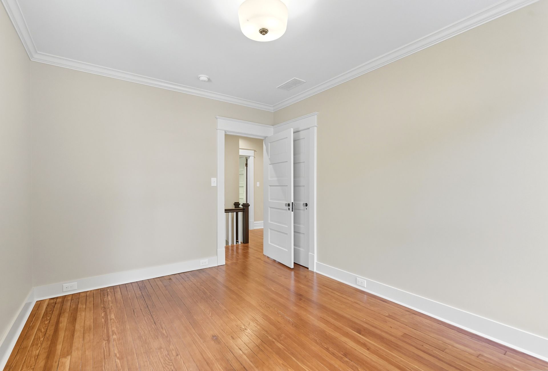 Empty room with hardwood floors, beige walls, white trim, and a doorway to another room.