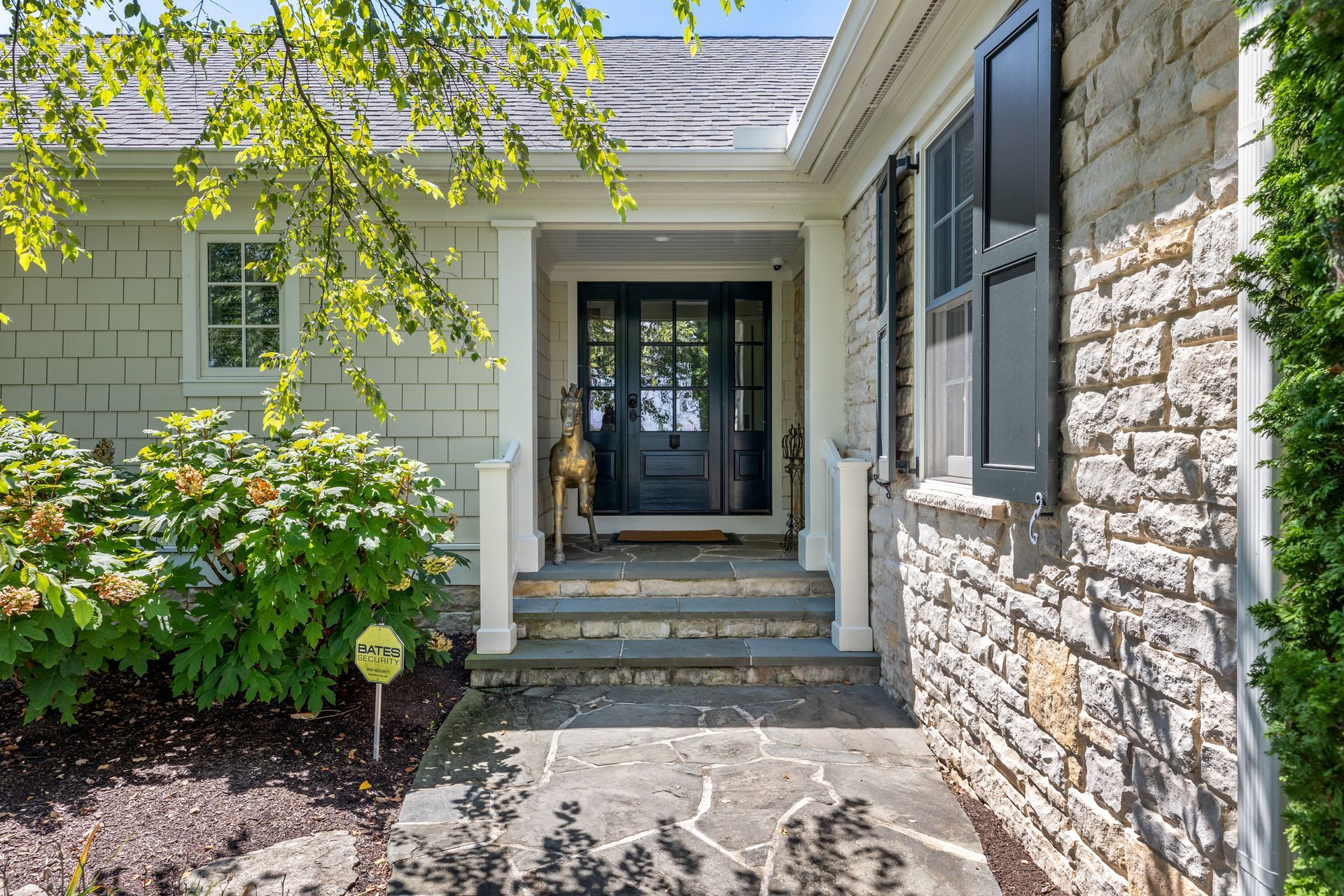 Stone house exterior with a black front door, steps, and landscaping.