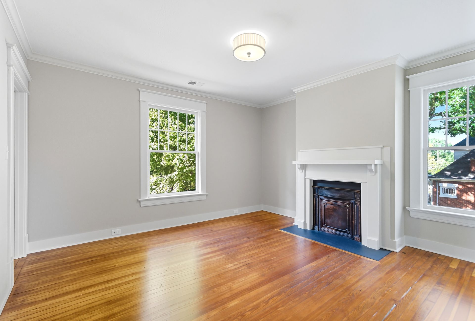 Empty room with hardwood floors, white walls, fireplace, and windows.