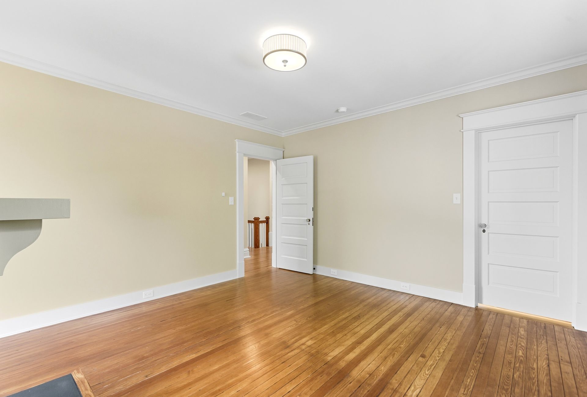 Empty room with wood floor, beige walls, white trim and doors, and a flush-mount ceiling light.