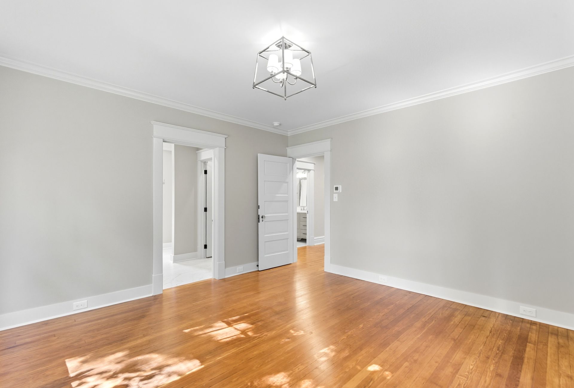 Empty room with hardwood floors, light gray walls, white trim, and a chandelier.