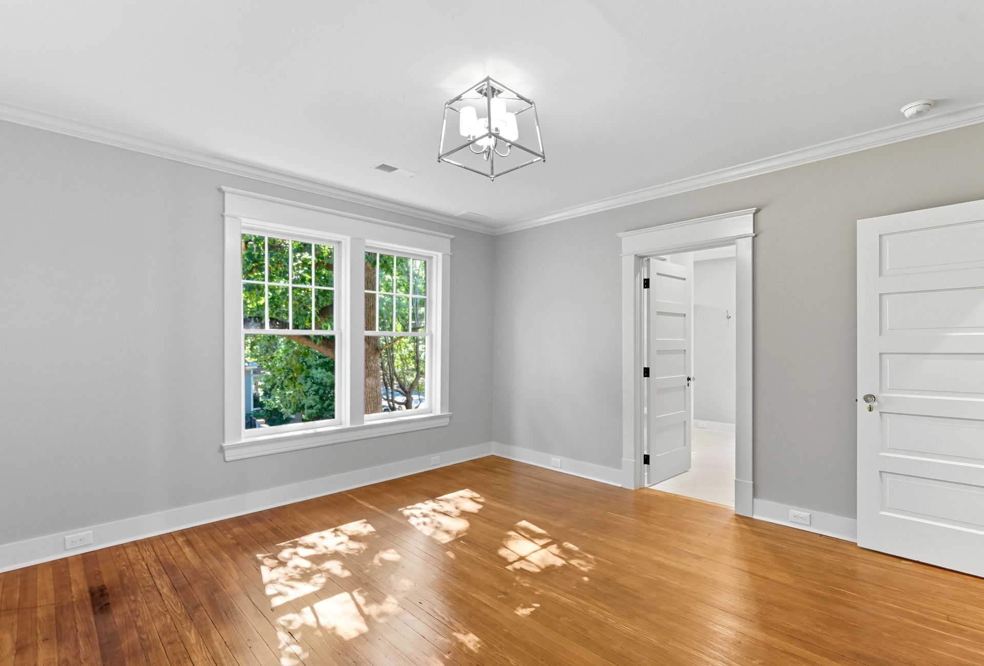 Empty room with hardwood floors, gray walls, white trim, and a window with sunlight.