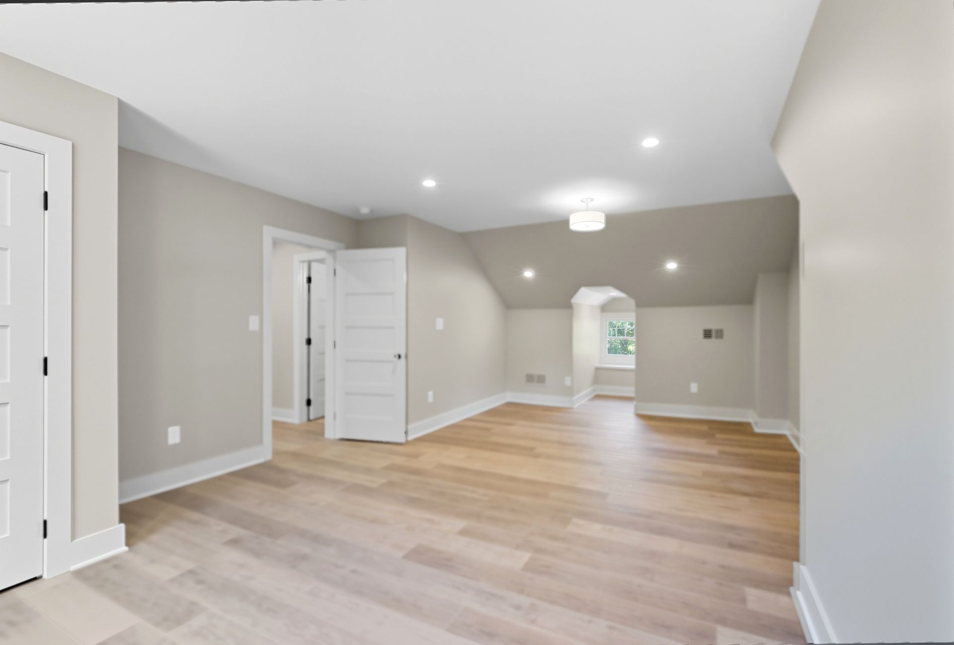 Spacious, light-filled room with light wood floors, neutral walls, and white doors.
