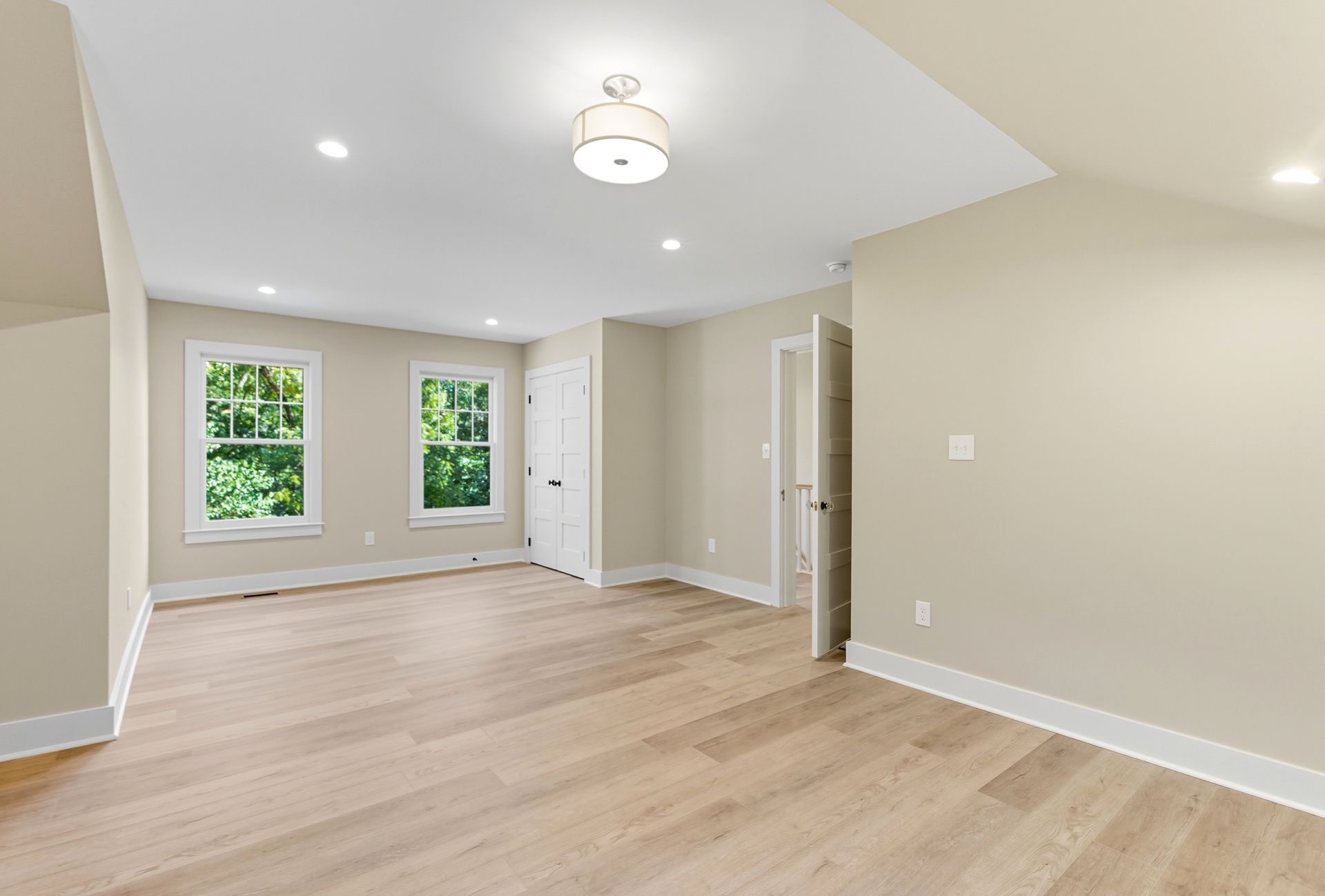 Empty, light-filled room with wood flooring, two windows, and neutral-colored walls.