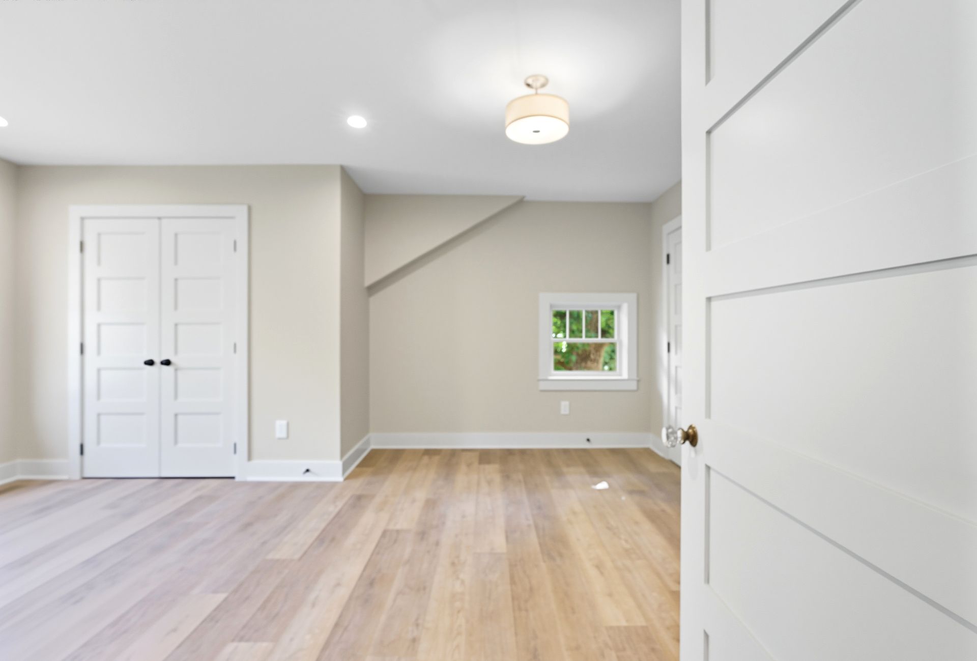 Empty room with hardwood floors, white walls, doors, and a window.