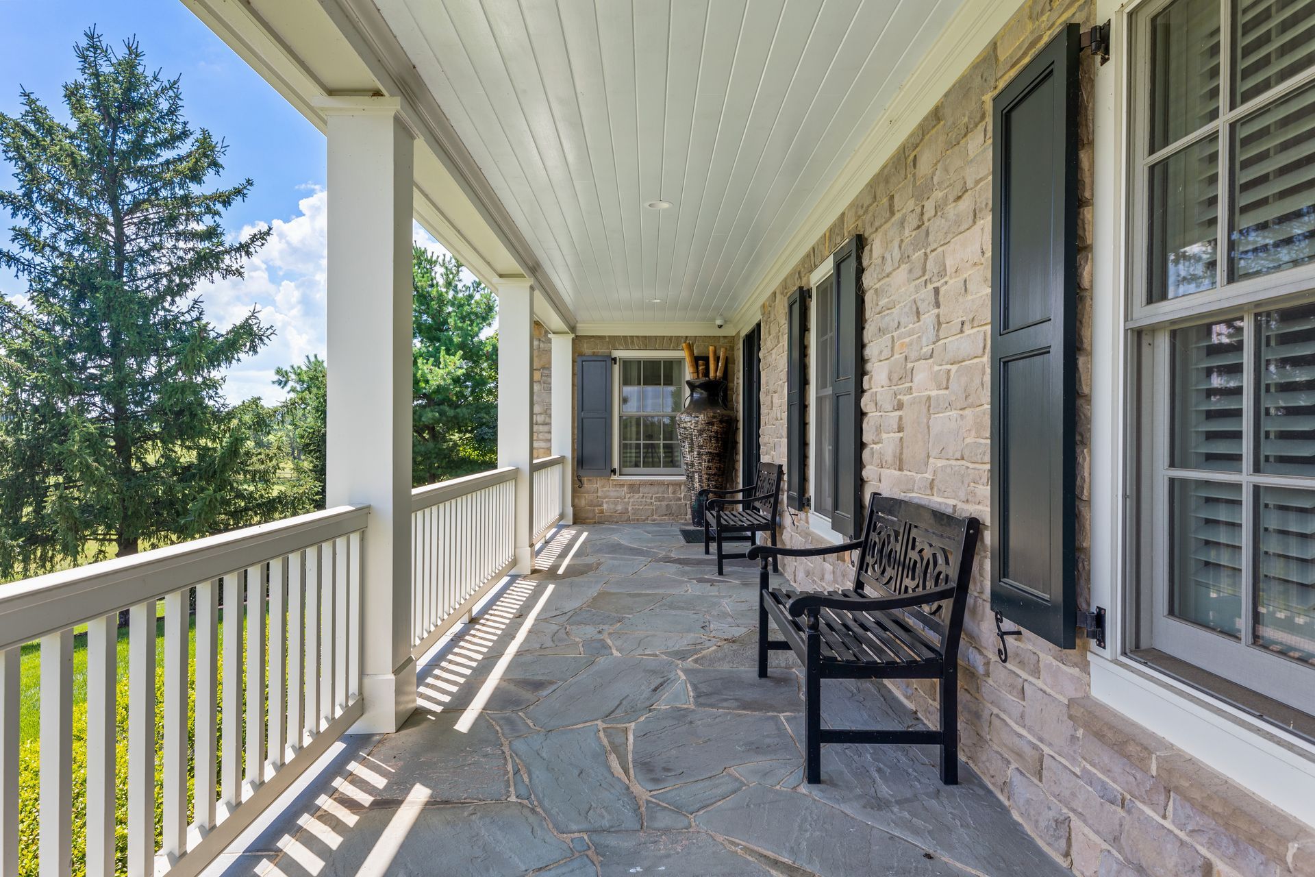 Covered porch with stone floor, benches, and brick wall with black shutters.
